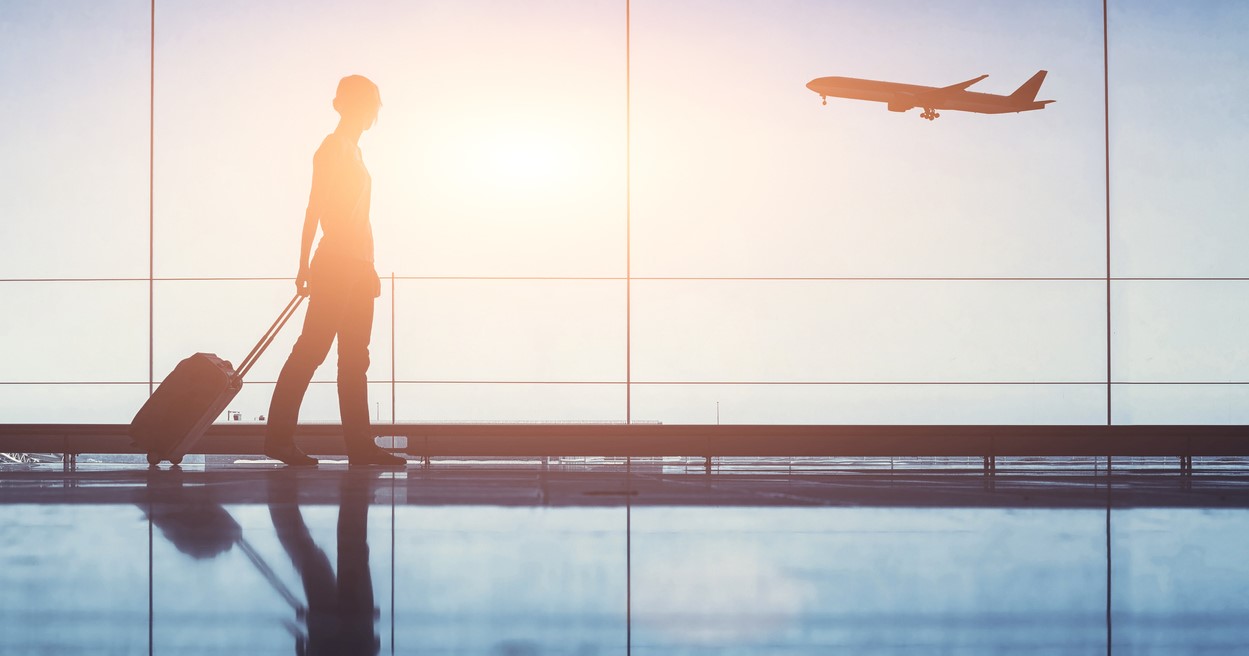 woman with suitcase at airport with plane taking off outside window