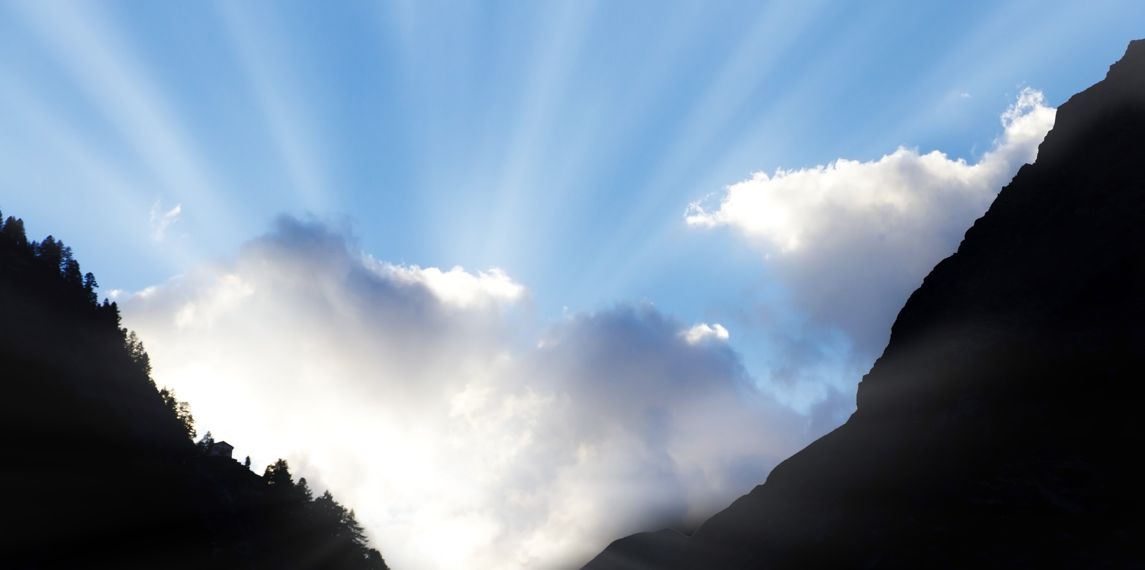 sun shining through clouds between two mountains